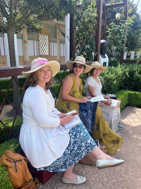 Three artists sitting on a bench at the Getty Villa with sketchbooks in their hands. 