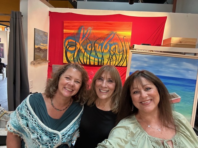 Kariba and two guests smiling in front of Kariba artwork in the art studio. 